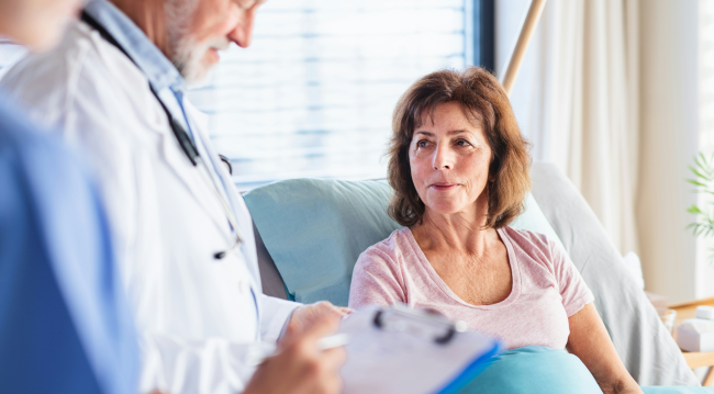 Personel medyczny rozmawia z osobą siedzącą na łóżku w placówce medycznej