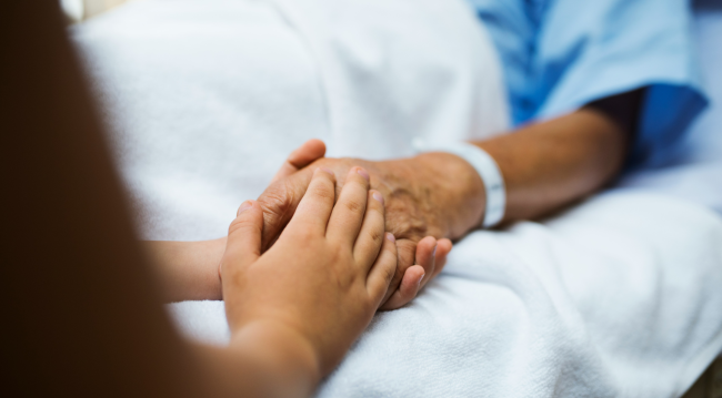 Bliska osoba trzyma za rękę osobę leżącą w łóżku